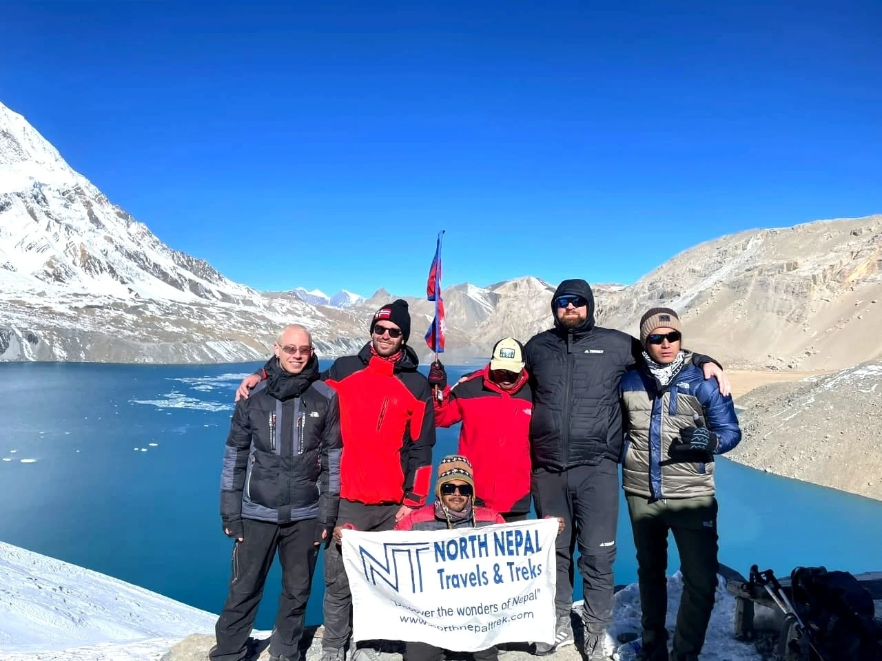 Trekkers from North Nepal trek clicking photo with banner with Tilicho lake as background during Annapurna Circuit Trek